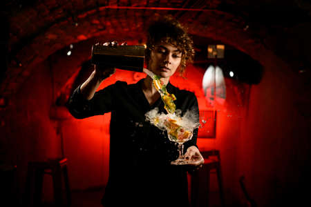 young attractive female barman pours cocktail from shaker into glassの写真素材