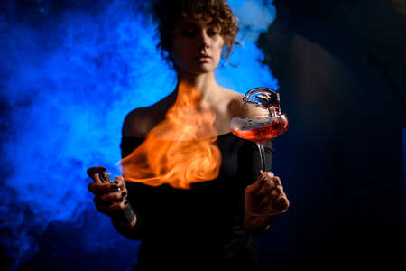 woman attentively holds glass with splashing drink, sprinkles and sets fire to it.の写真素材