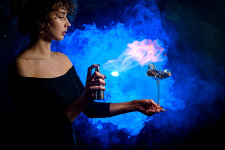 Young beautiful woman holds glass with splashing cocktail in front of her and sprinkles on itの写真素材