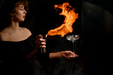 beautiful woman holds glass with splashing alcoholic cocktail sprinkles and make fire at it.