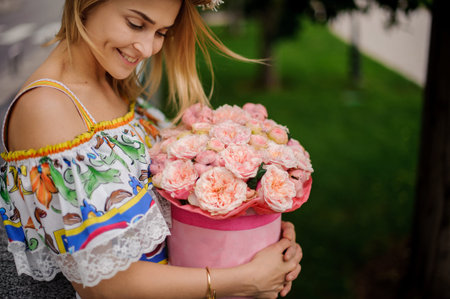 close-up. Smiling blond girl in colorful dress carefully holds round box with flowers