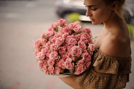 woman in beige dress gently holds bouquet with pink flowersの写真素材