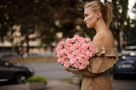 handsome woman gently holds bouquet with pink flowers and looks awayの写真素材