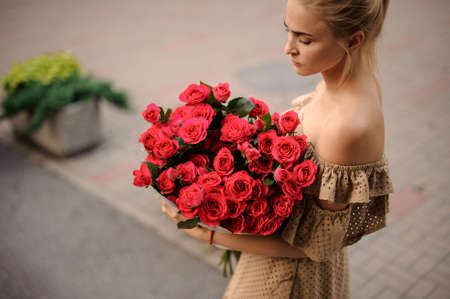 young blond woman holds large beautiful bouquet of red roses.の写真素材