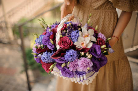 Beautiful white basket with flowers in purple tones in the hands of girl.の写真素材