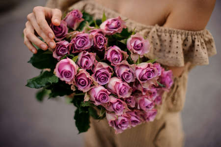 Close-up of bouquet of fresh purple roses in the hands of girlの写真素材