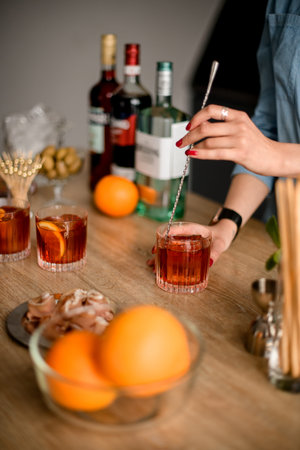 Woman stirs cocktail in glass with spoon on wooden kitchen table