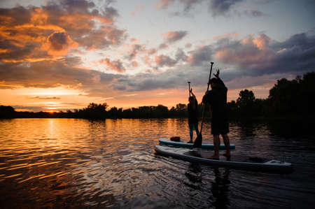 Couple of people on sup boards floating on the river at sunsetの写真素材