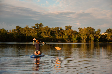 Rear view of woman which sits on sup board holds paddle and floats on the river