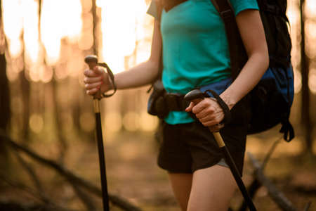 Close-up of young tourist woman with backpack and sticks in her hands in forest.の写真素材
