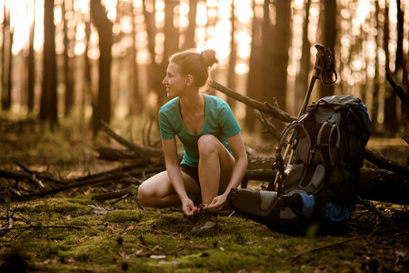 young woman in forest ties shoelaces on shoes and looks away.