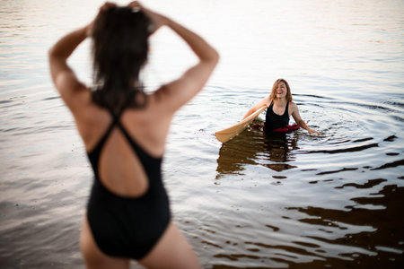 young smiling woman with surfboard comes out of the waterの写真素材