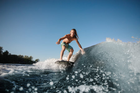 Tense and focused young man balancing on surfboard on river wave