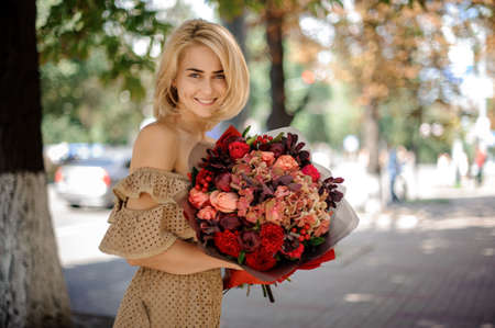smiling woman in beige dress holds in her hand bouquet of bright red flowers.の写真素材