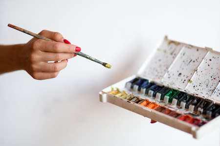 Womans hand with brush reaches for box with watercolor paints.の写真素材