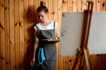 woman with paints stands on wooden wall background and looking downの写真素材