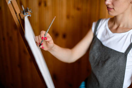 Closeup view of young artist who paints on canvas at wooden easel.の写真素材