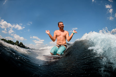 Cheerful man sitting on surfboard and shows a gesture with his hands