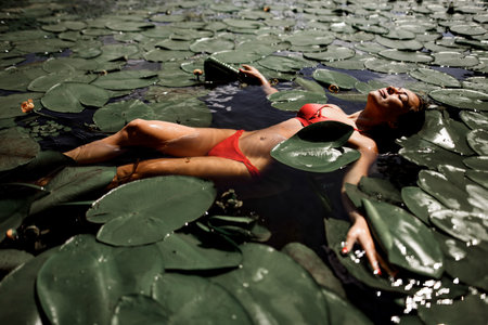 beautiful woman swimming in the pond among water lilies on sunny day.
