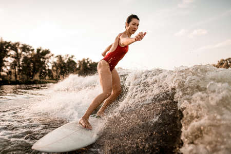 woman rides down on surfboard on river wave from boatの写真素材