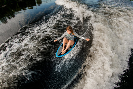 top view of blond woman who riding the waves while sitting on wakesurf board