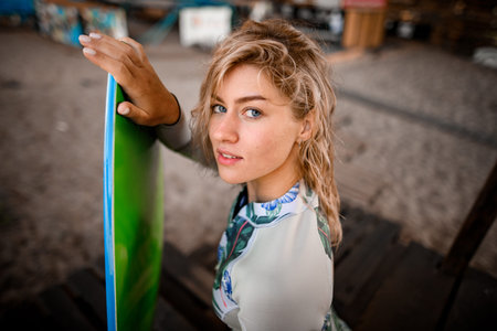 beautiful blonde woman sits on wooden pier and holds wakesurf board with her hand