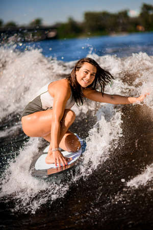 active woman wakesurfer balancing on surfboard along the wave.の写真素材