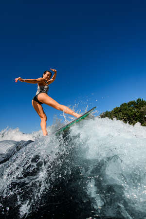 young wet woman energetically rides the wave on wakesurf boardの写真素材