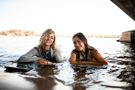 view of women in swimsuits who float on the river water on surfboards and looks at camera