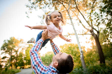 young father raises his handsome daughter high up with his handsの写真素材