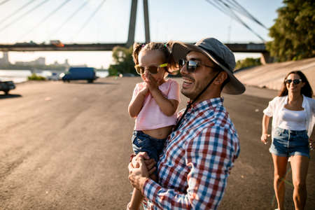 smiling young man in sunglasses holding little cute girl in his armsの写真素材