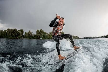 Athletic man having fun rides wave on surfboard in the summer day. Wakesurfing on Dnipro riverの写真素材