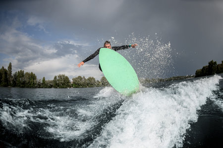 Strong man jumping on bright wakeboard on the wave of river