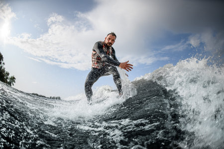 athletic man rides on surfboard down a wave and touches the water