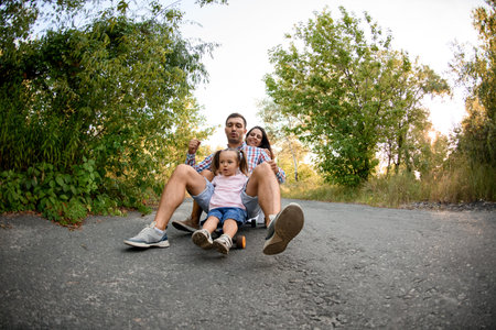 young mother father and little girl are sitting together on skateboard