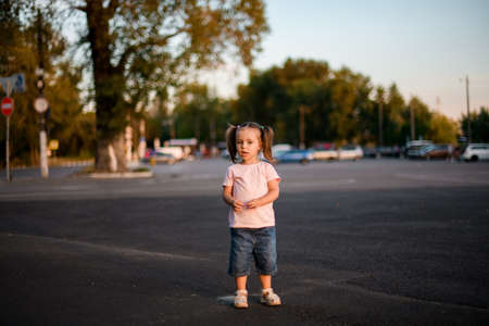 lovely little girl with blond hair stands alone on the roadの写真素材