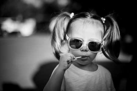 Black and white portrait of little cute girl in sunglasses with two ponytails.の写真素材