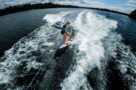 view of happy woman riding on the wake surf holding rope of motorboatの写真素材