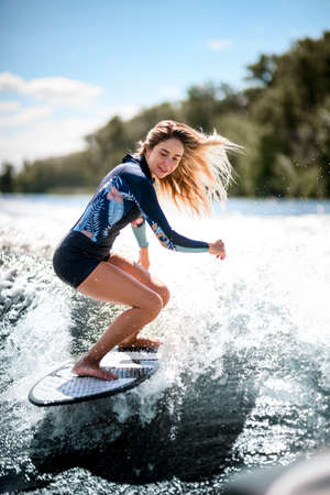 Beautiful woman stands with bent knees on surfboard and ride down on the splashing waveの写真素材