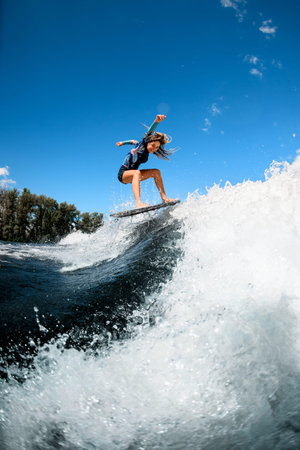 Beautiful young woman skillfully jumping with surf board on wave