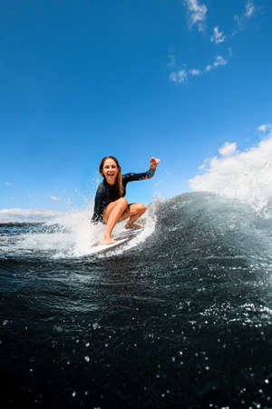 Beautiful view of happy woman sitting on surfboard and riding the waveの写真素材