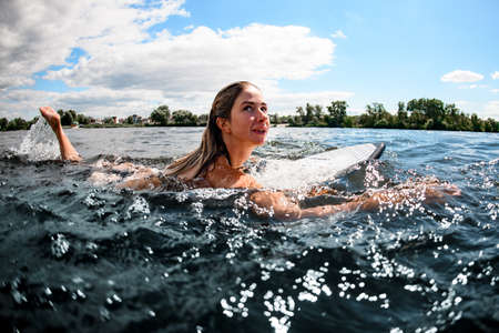 beautiful woman swims on the water with surfboard on sunny summer dayの写真素材