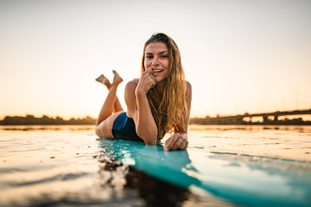 portrait of beautiful young smiling woman lies on surfboard on the water