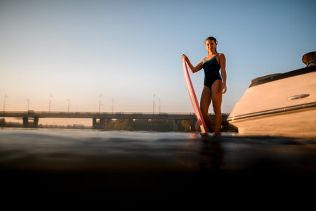 view of attractive woman in swimsuit with surf style wakeboard standing in the water.