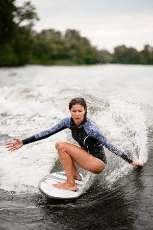wet woman stands with bent knees on a surfboard and ride down on the splashing wave