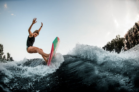 woman try to balance on surf style wakeboard on splashed river wave