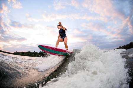 young athletic woman on surf style wakeboard and balances on big splashing wave