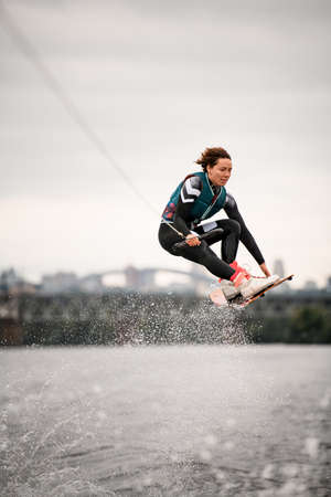 woman in wetsuit holding rope and professionally jumping over water on wakeboardの写真素材