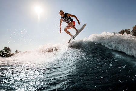 view of man jumping over river wave on board against sunny blue sky.の写真素材