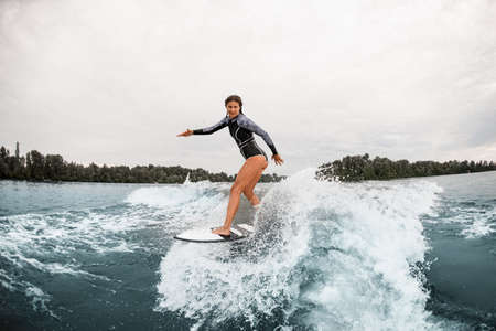 attractive woman in black wetsuit stand on a surfboard and rides on waveの写真素材